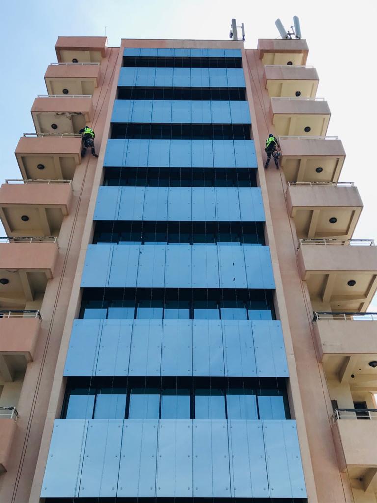 Two ECEP Ltd workers rappelling to install curtain-wall cladding panels on a high-rise